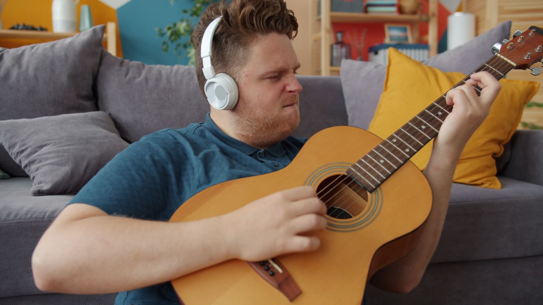 Un hombre con auriculares toca una guitarra acústica en un salón acogedor.