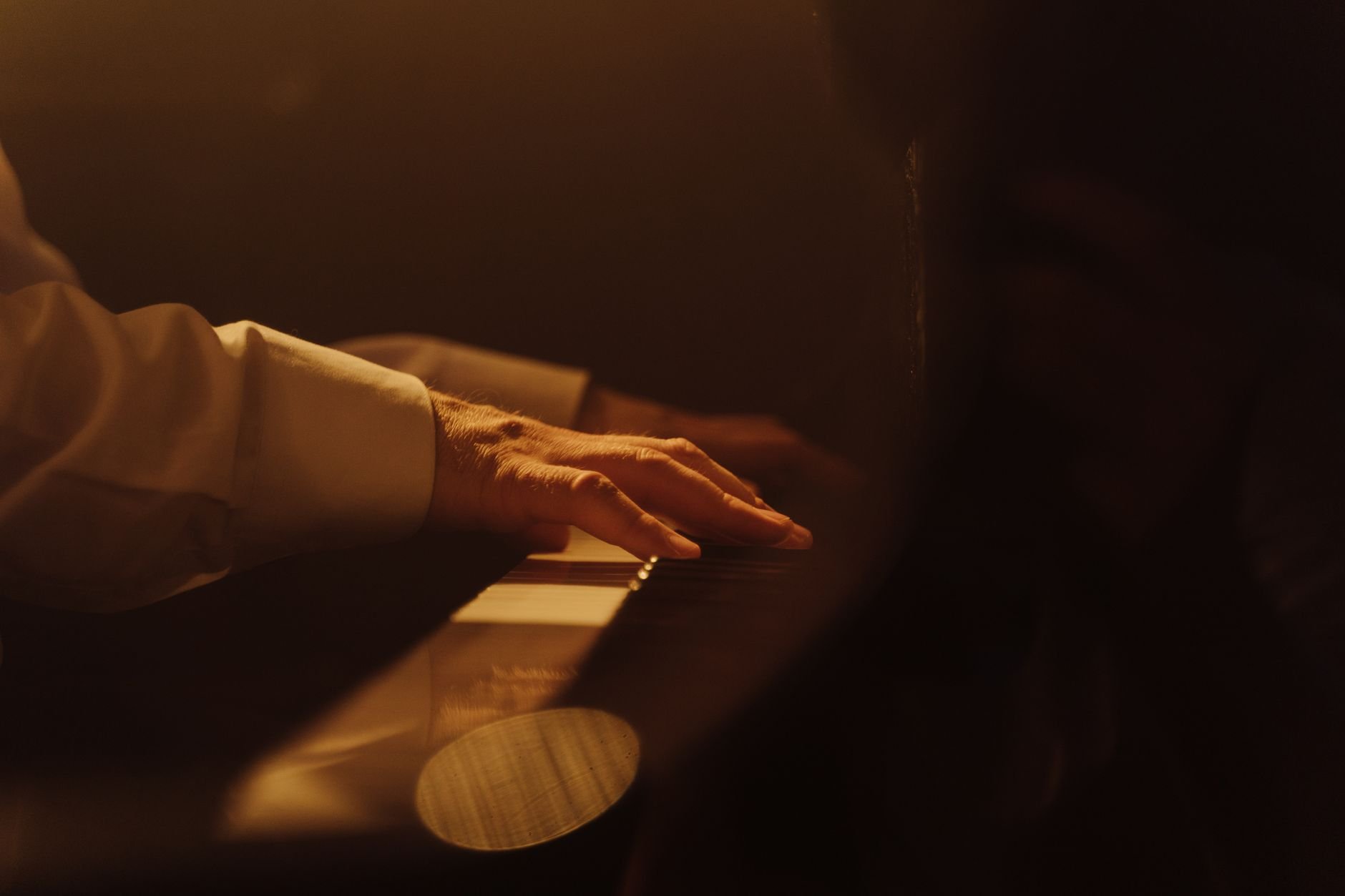 Primer plano de una mano tocando el piano con luz cálida.